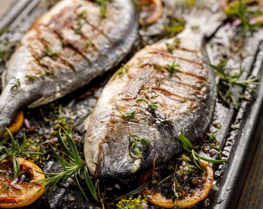 Grilled fish with herbs and lemon on a grill plate, close up view. Grilled sea bream, barbecue clipart