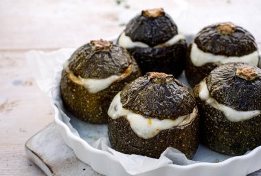 Vejetaryen Kabak dolması. Pişmiş yuvarlak kabak dolması pirinç, mantar ve peynir bir ahşap beyaz masa üzerinde bir pişirme çanağı aromatik otlar ilavesi ile