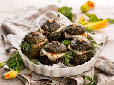 Vejetaryen Kabak dolması. Pişmiş yuvarlak kabak dolması pirinç, mantar ve peynir bir ahşap beyaz masa üzerinde bir pişirme çanağı aromatik otlar ilavesi ile