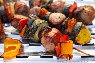 Grilled skewers of meat, sausages and various vegetables on a grill plate, outdoors.  Grilled food, bbq clipart