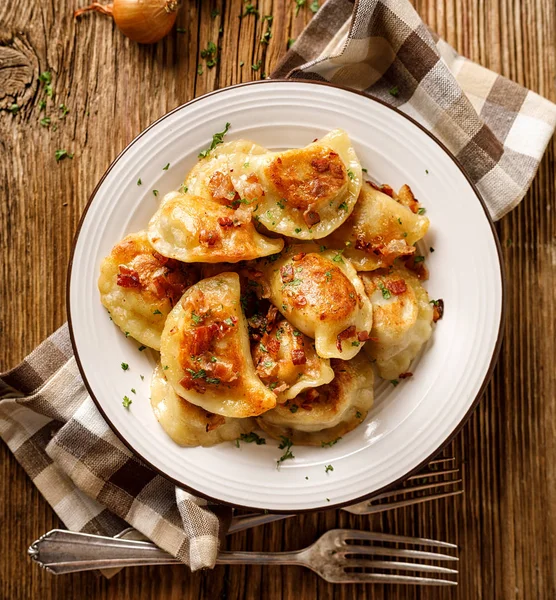 Fried dumplings stuffed with cabbage and meat sprinkled with bacon greaves and chopped parsley on a white plate on a wooden rustic table, top view. — Stock Image Fried Dumplings Stuffed Cabbage Meat Sprinkled Bacon Greaves Chopped Parsley Royalty Free Stock Images