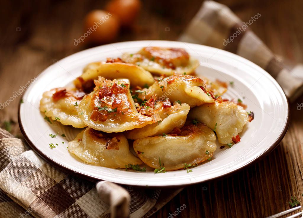 Fried dumplings stuffed with cabbage and meat sprinkled with bacon greaves and chopped parsley on a white plate on a wooden rustic table.