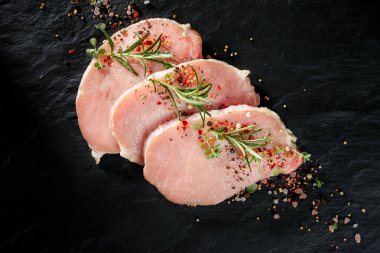 Çiğ domuz loin dilimleri aromatik otlar ve baharatlar siyah taş zemin, üstten görünüm eklenmesi ile