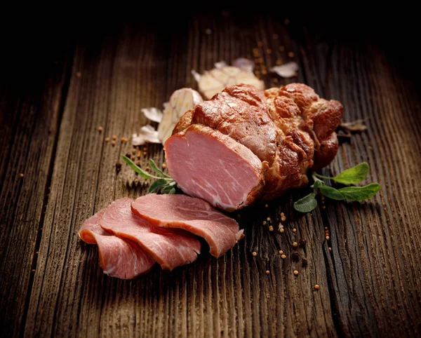 Smoked meat, Sliced smoked gammon on a wooden  table with addition of fresh  herbs and aromatic spices.   Natural product from organic farm, produced by traditional methods