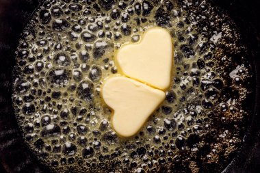 Fried butter, a piece of butter in the shape of hearts, fried on a black cast-iron pan. Impression about a healthy heart, anti cholesterol prophylaxis, healthy heart concept clipart