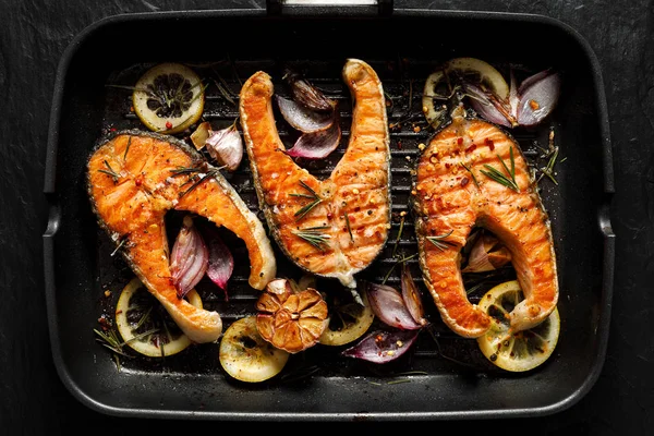 Grilled fish, grilled salmon steak  with addition of lemon, rosemary, garlic, onion and spices on grill plate, top view. 