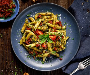 Ispanak ile penne makarna, Güneş kurutulmuş domates ve tavuk, bir seramik plaka üzerinde parmesan peynir ve taze maydanoz serpilir, üst görünüm.