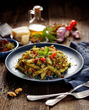 Ispanak ile penne makarna, Güneş kurutulmuş domates ve tavuk, bir seramik plaka üzerinde parmesan peynir ve taze maydanoz serpilir.