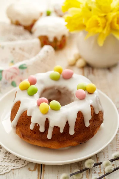Easter yeast cake (Babka) covered with icing and decorated with marzipan eggs on a white plate on a wooden table. Traditional Easter cake in Poland
