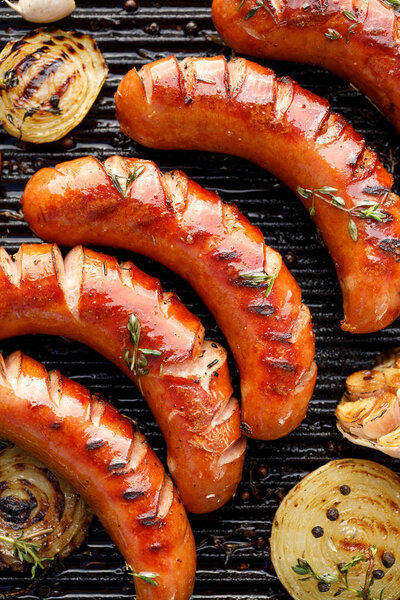 Grilled sausage with the addition of herbs and vegetables on the grill plate, close-up, top view. Grilling food, bbq, barbecue grill