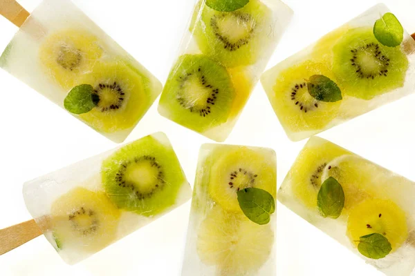 Fruit popsicles, homemade fruit ice lolly of various fruits; kiwi fruit and lime with the addition of fresh mint and citrus lemonade on a white background, top view. Delicious healthy desert