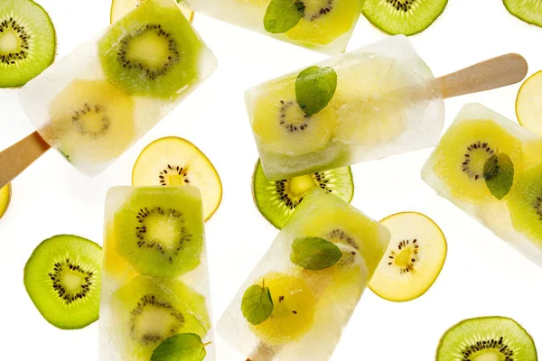 Fruit popsicles, homemade fruit ice lolly of various fruits; kiwi fruit and lime with the addition of fresh mint and citrus lemonade on a white background, top view. Delicious healthy desert