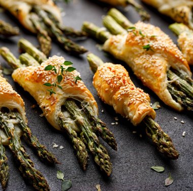 Siyah bir arka planda, yakın çekim susam, Nigella tohumları ve taze kekme ile serpilir puf pasta pişmiş yeşil kuşkonmamış. Puf pasta demetleri