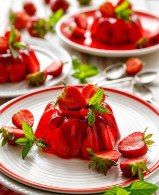 Beyaz bir tabakta taze çilek ve nane yaprağı eklenmiş çilek jölesi, yakın çekim. Meyveli tatlı.