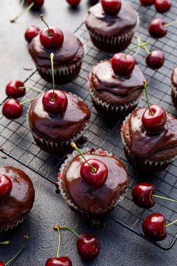 Eritilmiş koyu çikolata kaplı çikolatalı kekler ve soğutma tepsisinde taze kiraz. 