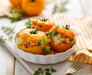 Domates dolması, beyaz ahşap bir masa üzerinde bir fırın kabına aromatik otlar ilavesi ile bulgur, sebze ve peynir ile doldurulmuş pişmiş sarı domates. Vejetaryen yemekler