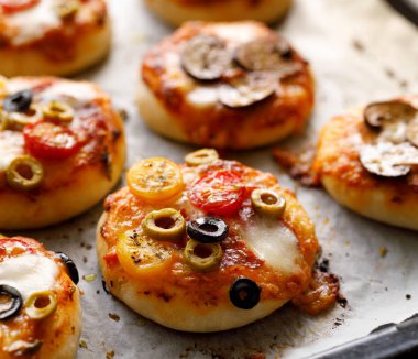 Ek sebze çeşitli mini pizzalar, mozzarella peyniri ve taze fesleğen beyaz fırın kağıdı, yakın çekim.