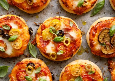 Ek sebze çeşitli ile küçük vejetaryen pizzalar, mozzarella peyniri ve taze fesleğen beyaz fırın kağıdı, yakın çekim, üst görünümü.