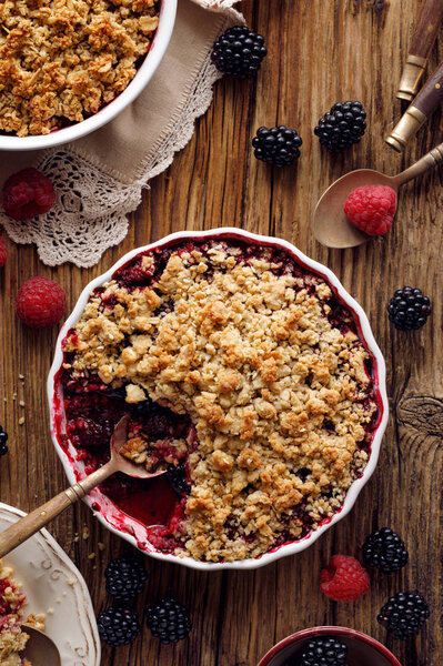Crumble, Mixed berry (blackberry, raspberry) crumble, stewed fruits topped with crumble of oatmeal, almond flour, butter and sugar  in a baking dish on a wooden table, top view