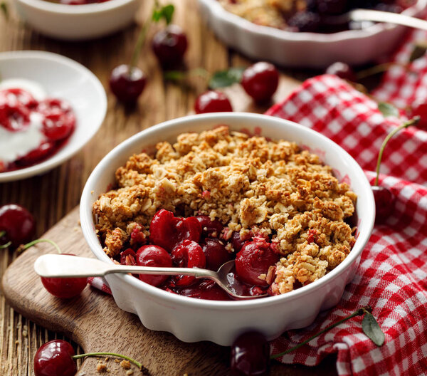 Cherry crumble in a baking dish on a wooden table, close-up