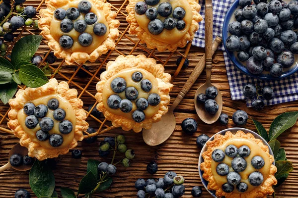 Small tarts made of puff pastry with addition fresh blueberries and caramel chocolate custard on a wooden rustic table, top view, close up. Delicious homemade dessert or breakfast