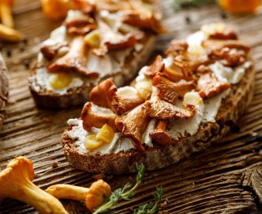 Açık yüzlü sandviç, chanterelle mantarlı mantarlı mantarlı sandviç, tahta rustik bir masada kremalı keçi peyniri ve sarımsak, yakın çekim.