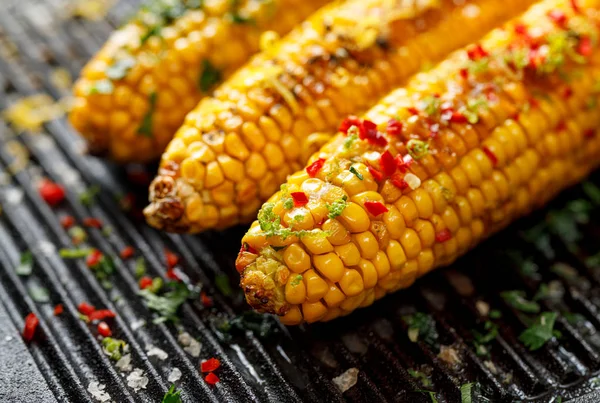 Grilled corn on the cob with butter, herbs, salt and aromatic spices on the grill plate, close-up