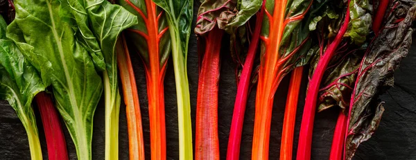 Swiss chard in different colors, multi colored  stems on a black background, top view