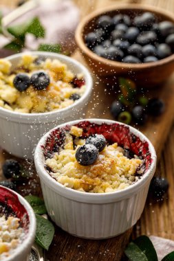 Yaban mersini ufalamak, haşlanmış bilberries bir ahşap masa üzerinde bir fırın kabına ufalanmış toz şeker serpilir ile tepesinde, yakın çekim. Ev yapımı meyve tatlısı