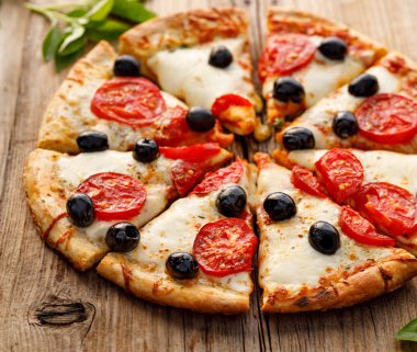 Mozzarella peyniri, domates ve siyah zeytin ile Pizza, ahşap bir arka plan üzerinde parçalar halinde kesilmiş, yakın. İtalyan yemekleri