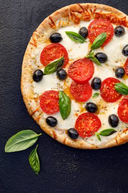 Pizza domates, mozzarella peyniri, siyah zeytin ve siyah bir arka plan üzerinde taze fesleğen, yakın çekim, üst görünümü. İtalyan yemekleri