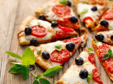 Domates, siyah zeytin, mozzarella peyniri ve ahşap bir arka plan üzerinde taze fesleğen ile dilimlenmiş pizza, yakın. İtalyan yemekleri