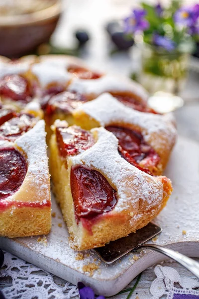 Plum cake, traditional homemade  cake with fruit, divided into portions, sprinkled with powdered sugar on a white board, close-up view. Fruit cake, dessert