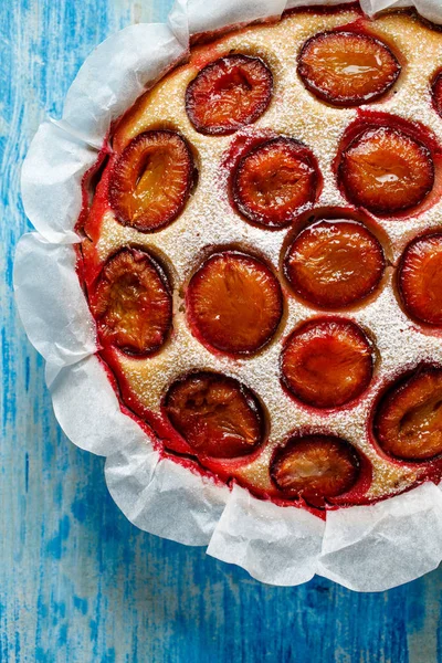 Plum cake, traditional homemade  cake with sweet plums, sprinkled with powdered sugar on a blue wooden table, top view, close-up. Fruitcake, delicious dessert