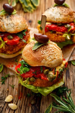 Vejetaryen hamburgerler, ızgara biberli balkabağı burgerler, taze marul, aromatik otlar ve ahşap kırsal bir masada kapari, yakın çekim.