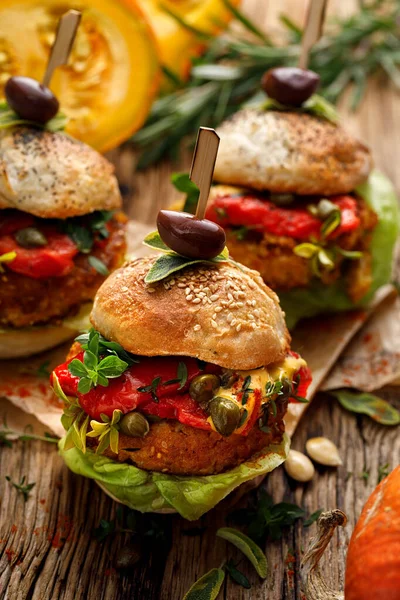 Pumpkin burgers with the addition of grilled peppers, fresh lettuce, herbs and capers on a wooden rustic background, close-up. Vegan burgers