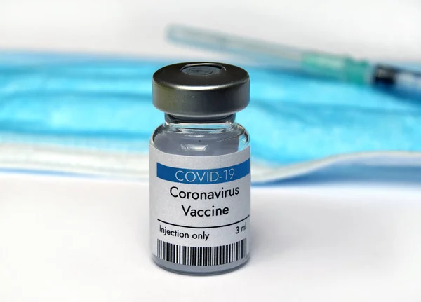 Coronavirus vaccine vial with syringe and face mask. Close-up on white background.
