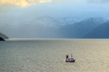 Norveç fiyortunun içindeki küçük balıkçı teknesinde dağda kar var.