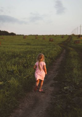 Mutlu bir çocuk gün batımında samanlıkların arasında koşar.