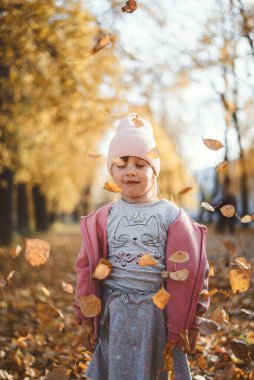 Bir çocuk sonbaharda yapraklarla oynar