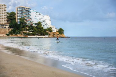 bir kumsalı ile bir açık deniz dalga ve denizin bir bulutlu gökyüzü karşı yalnız bir sörfçü bir parçası