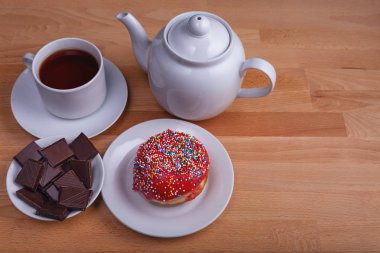 bir fincan çay ve gıda arka plan olarak bir tabak üzerinde çikolata parçaları ile iştah açıcı bir donut