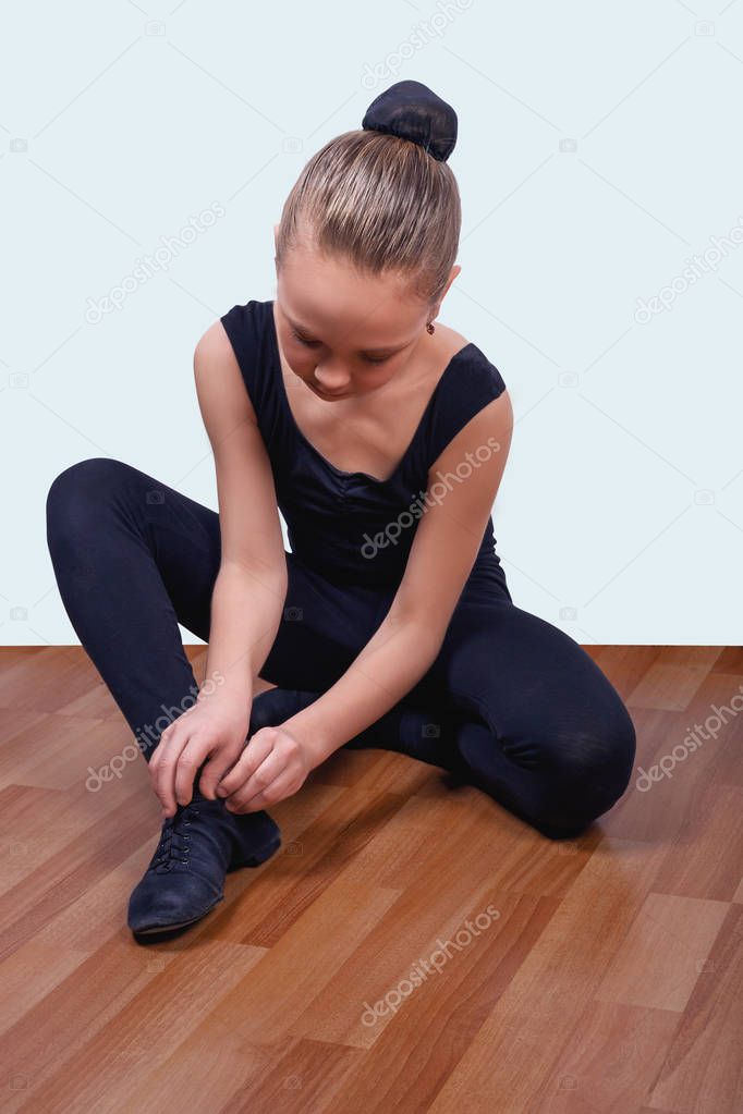 student of ballet school tying shoelaces on shoes before clas