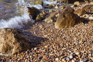 küçük ve büyük taşlar ve hareketli bir deniz dalgası ile güneşli bir kayalık plaj parçası