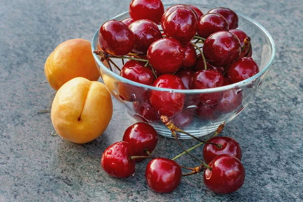 ripe red cherries and apricots on a stone surface in the rays of the setting sun