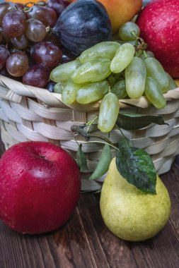 Kırmızı üzümler ve taze meyveler siyah ahşap bir sırtüstü saman sepetinde