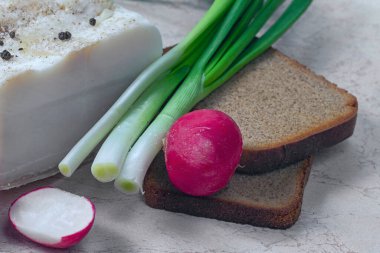 Ekmek, tuzlanmış pastırma, turp ve soğanlı ahşap masa.