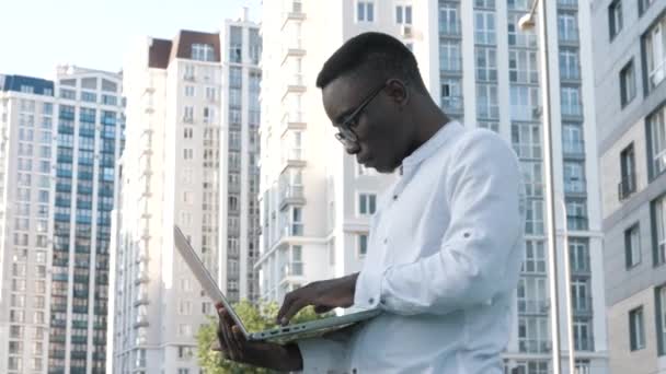 Young black man freelancer student using laptop studying online working outdoors in internet, focused millennial african american guy typing on computer surfing web looking at screen — Stock Video