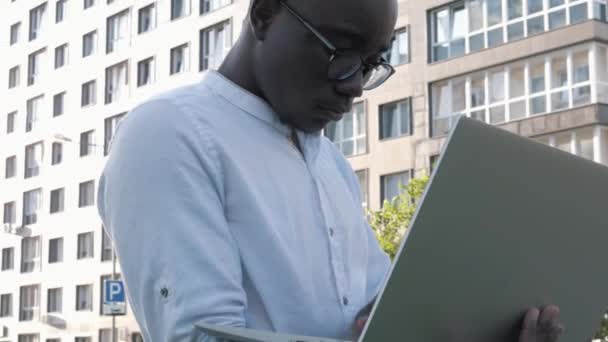 Joven hombre negro freelancer estudiante utilizando el ordenador portátil que estudia en línea trabajando al aire libre en Internet, enfocado millennial africano americano empresario escribiendo en la web de navegación por ordenador mirando a la pantalla disfrutando — Vídeos de Stock