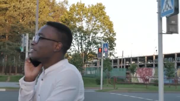 Closeup smiling happy black man talking mobile phone outdoors. Close up of cheerful african american businessman having phone call, business conversation while crossing a road — Stock Video